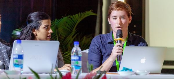 Three people sitting at a table with laptops engaged in discussion