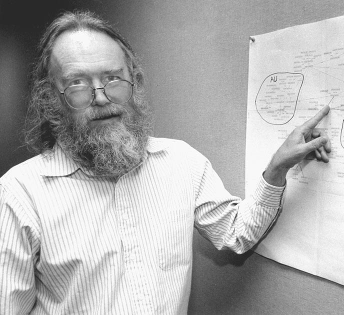 a man with a beard and glasses pointing to a board