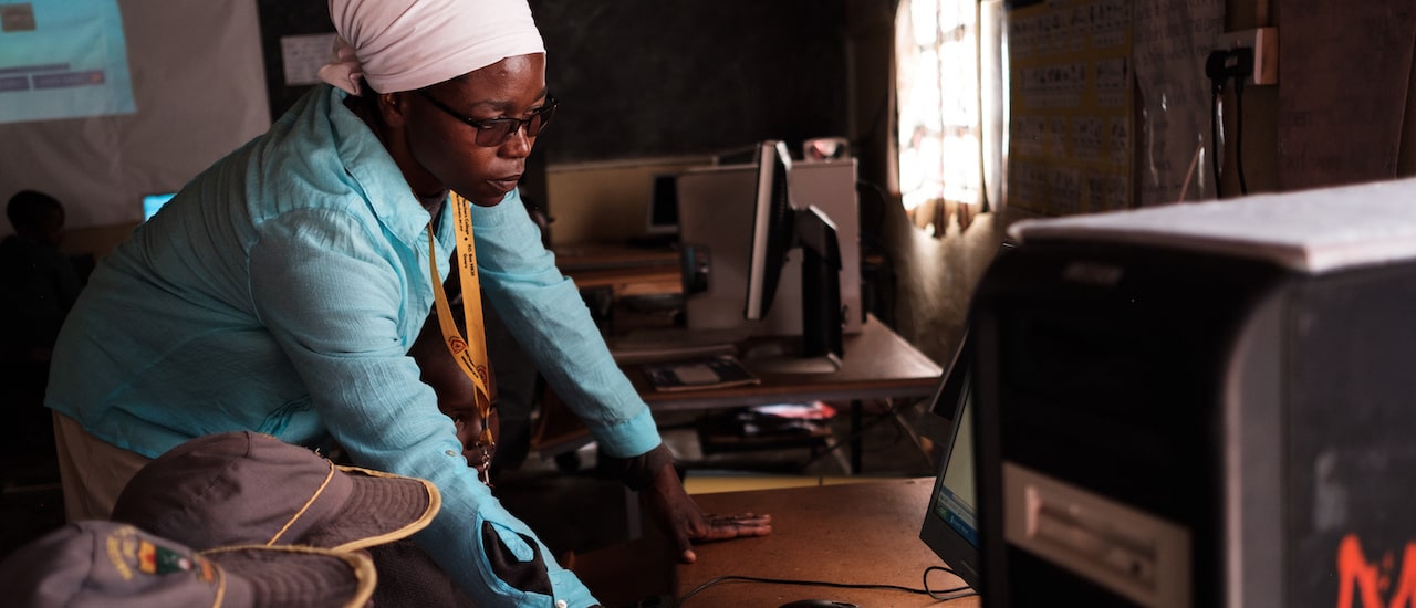 a woman stands and explains the lesson to a student in front of computer screen