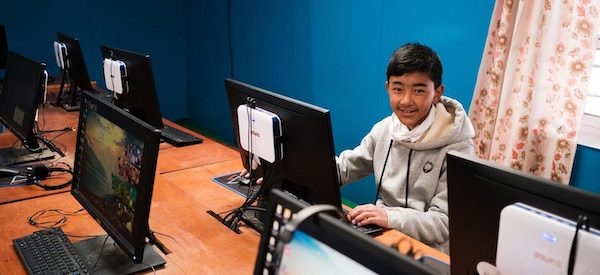 a boy sitting in front of the computer in a classroom smiling